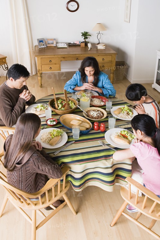 Family with three children (8-9, 10-11) praying at table before dining. Photo: Rob Lewine