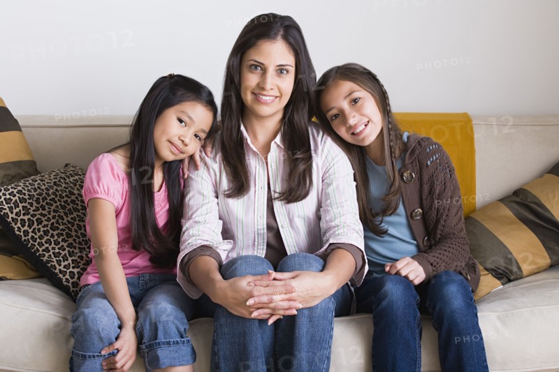 Portrait of happy mother with two daughters (8-9, 10-11) sitting on sofa. Photo: Rob Lewine