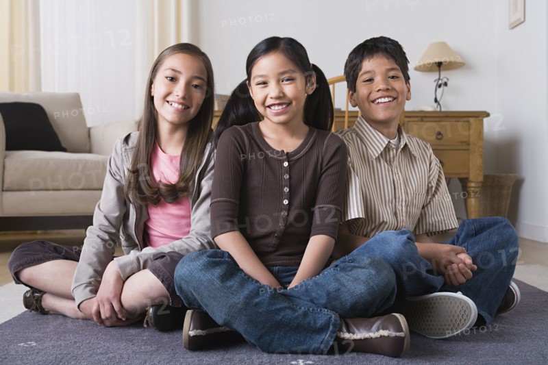 Portrait of happy children (8-9, 10-11) sitting on floor. Photo : Rob Lewine