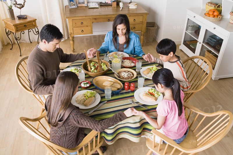 Family with three children (8-9, 10-11) praying at table before dining. Photo: Rob Lewine
