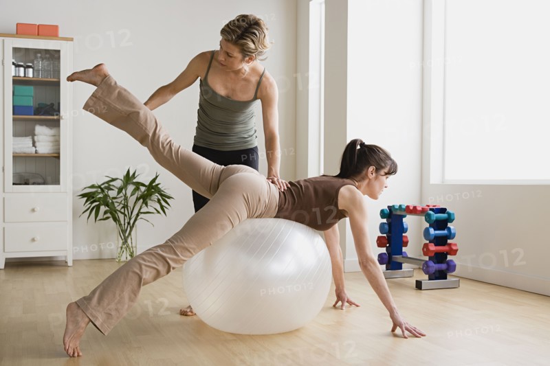Woman assisting another woman in exercise with fitness ball. Photo : Rob Lewine