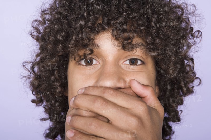 Portrait of teenage boy (14-15) covering mouth with hands. Photo: Rob Lewine
