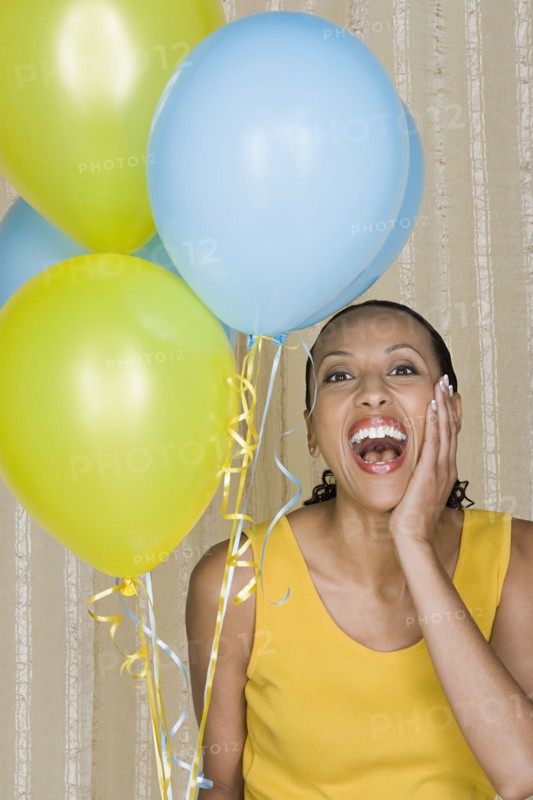 Happy mid adult african woman shouting while holding yellow and blue balloons. Photo : Rob Lewine