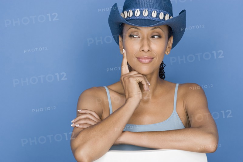 Portrait of mid adult woman sitting on white chair, wearing blue cowboy hat. Photo : Rob Lewine