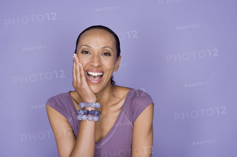 Portrait of smiling woman sitting on purple background, studio shot. Photo : Rob Lewine