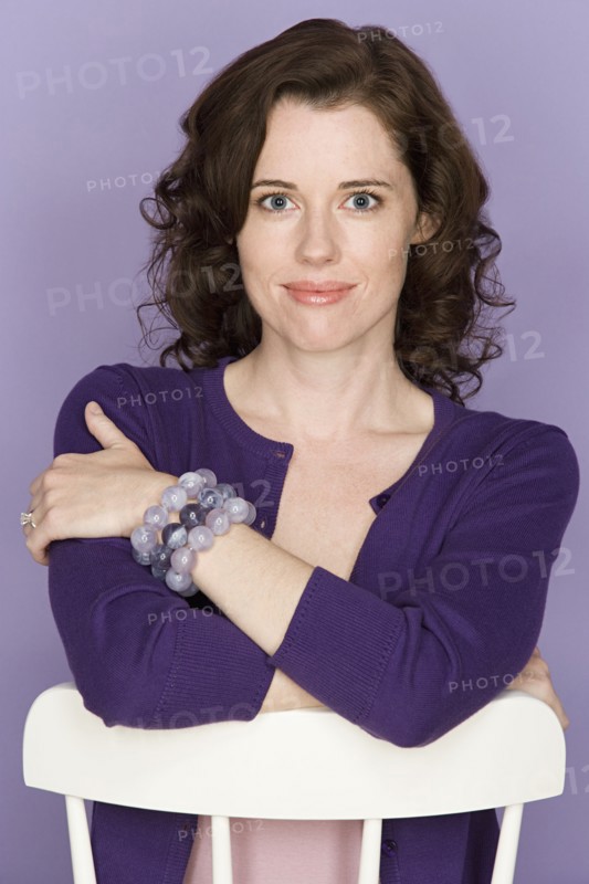 Portrait of smiling woman sitting on chair with purple background, studio shot. Photo : Rob Lewine