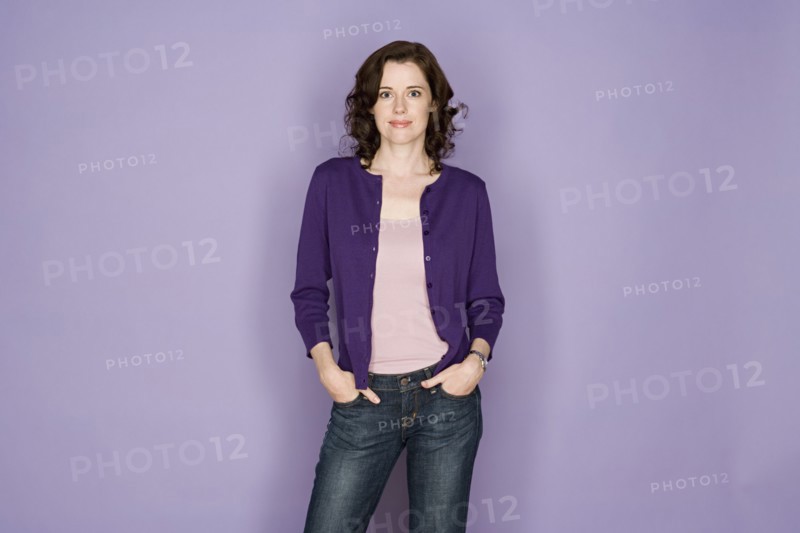 Portrait of smiling woman on purple background, studio shot. Photo : Rob Lewine