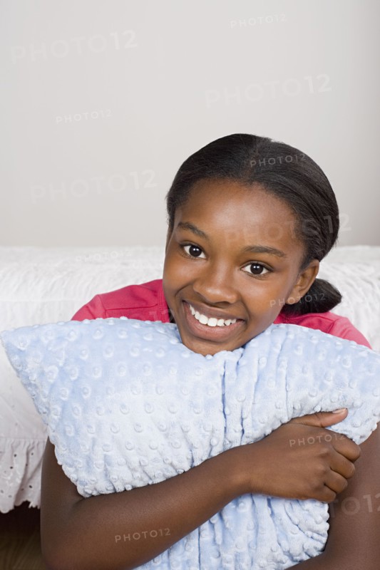 Portrait of smiling girl (10-11) with pillow. Photo : Rob Lewine