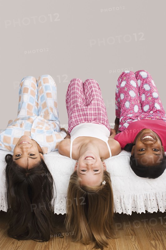 Portrait of three girls (10-11) lying on bed with heads down . Photo: Rob Lewine