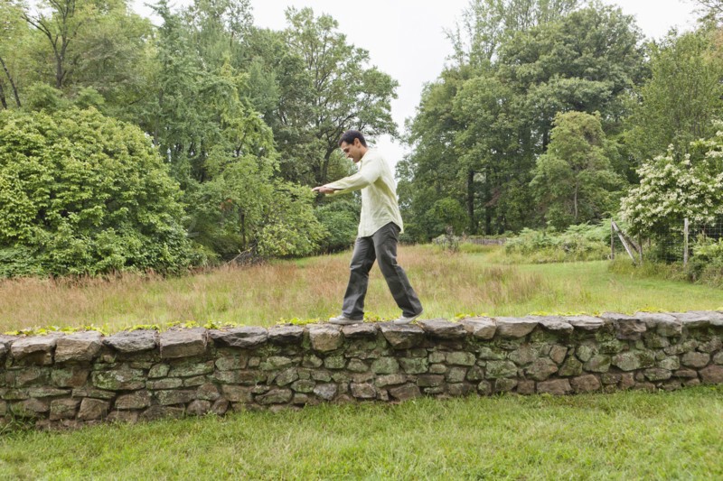USA, New Jersey, Man walking on stone wall on field. Photo: Tetra Images