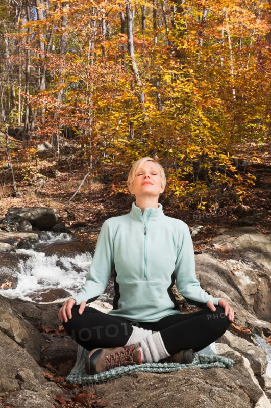 Woman meditating by stream in forest. Photo : Tetra Images