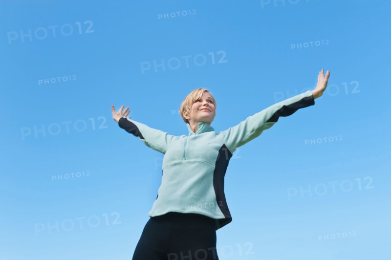 Woman with arms raised against blue sky. Photo : Tetra Images