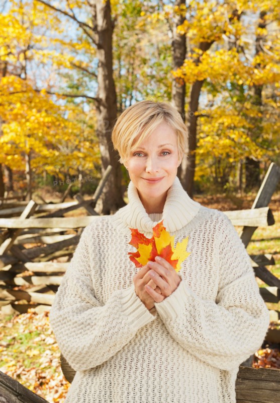 Portrait of smiling woman holding leaves in Autumn forest. Photo : Tetra Images