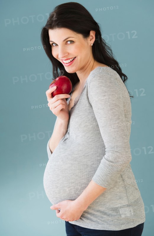 Studio portrait of pregnant woman eating apple.