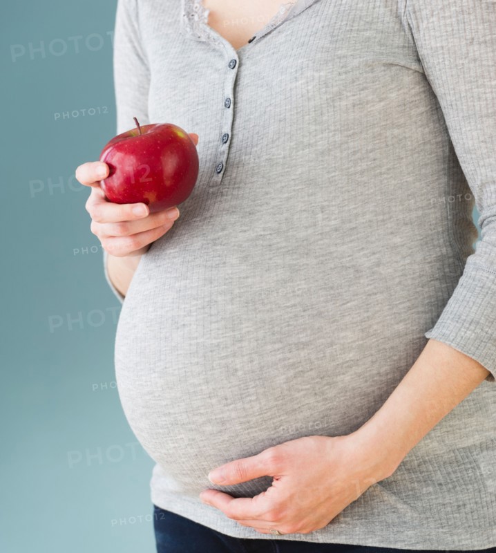 Studio shot of pregnant woman eating apple, midsection.