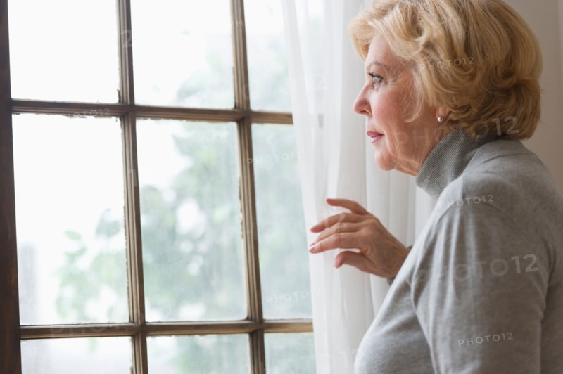 Portrait of senior woman looking through window.