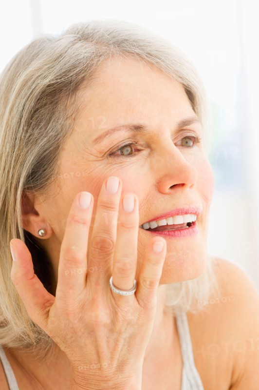 Portrait of senior woman applying moisturizer.