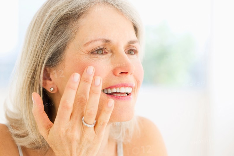 Portrait of senior woman applying moisturizer.