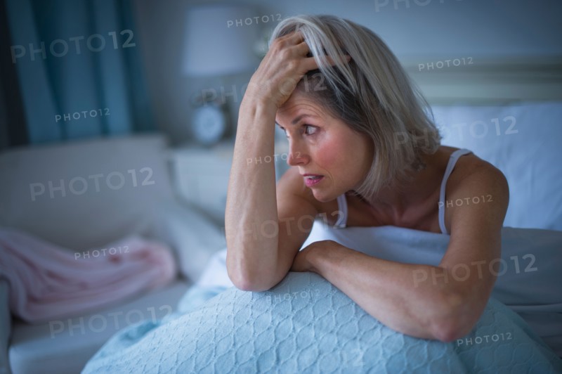 Senior woman sitting in bed and suffering from insomnia.