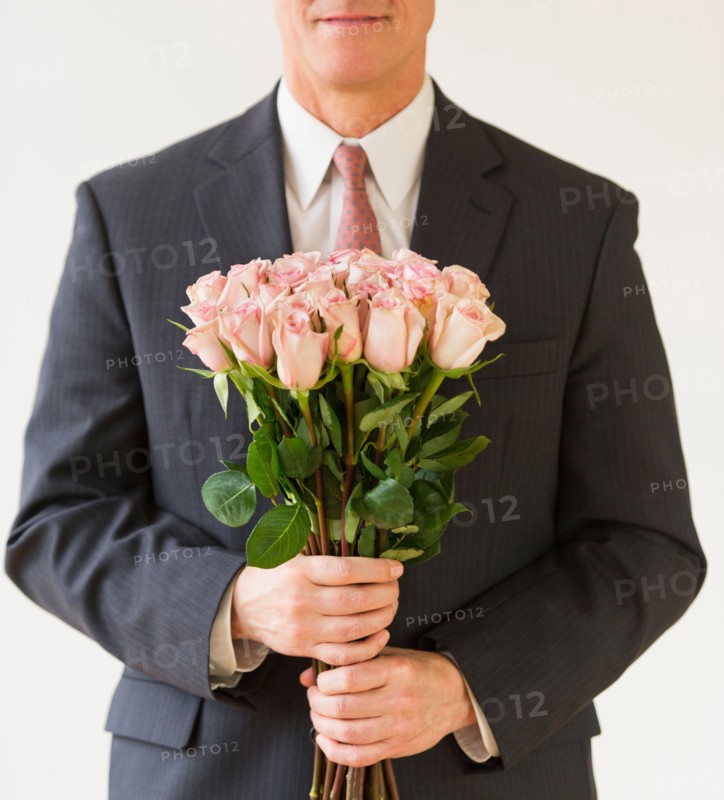 Close up of man in suit holding bouquet of roses, studio shot.