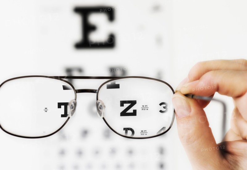 Close up of hand holding glasses above eye chart, studio shot.