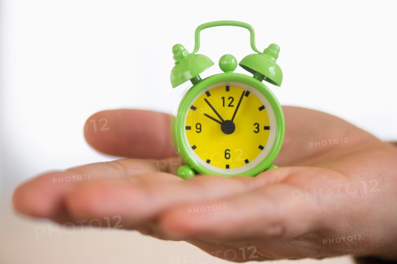 Close up of man's hand holding alarm clock, studio shot.