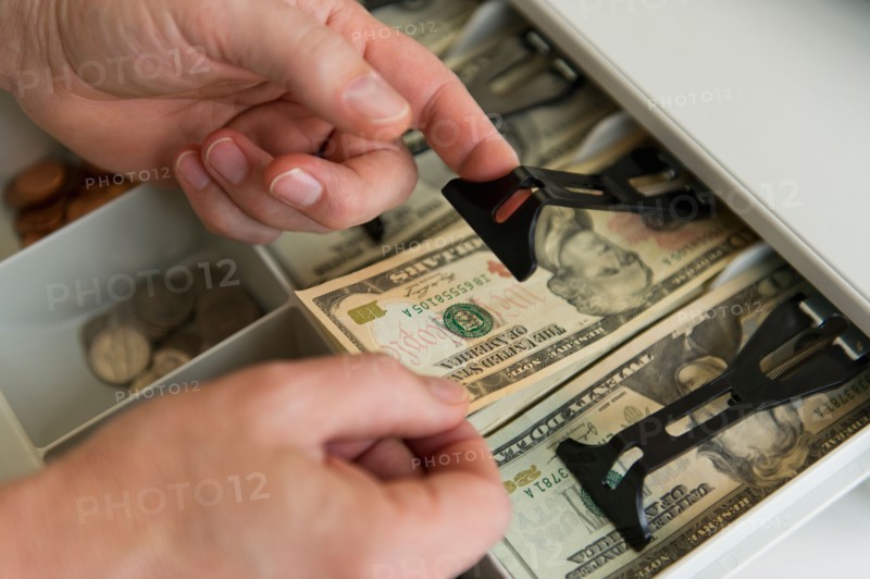 Close up of man's hand putting banknotes into cash register, studio shot.