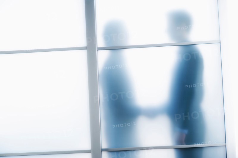 Silhouettes of two businessmen behind glass door.