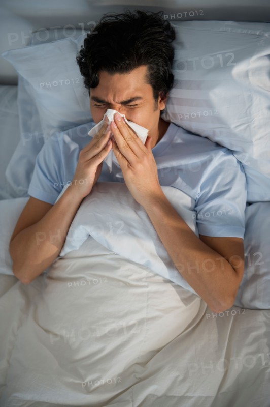 Man lying in bed and blowing nose.
