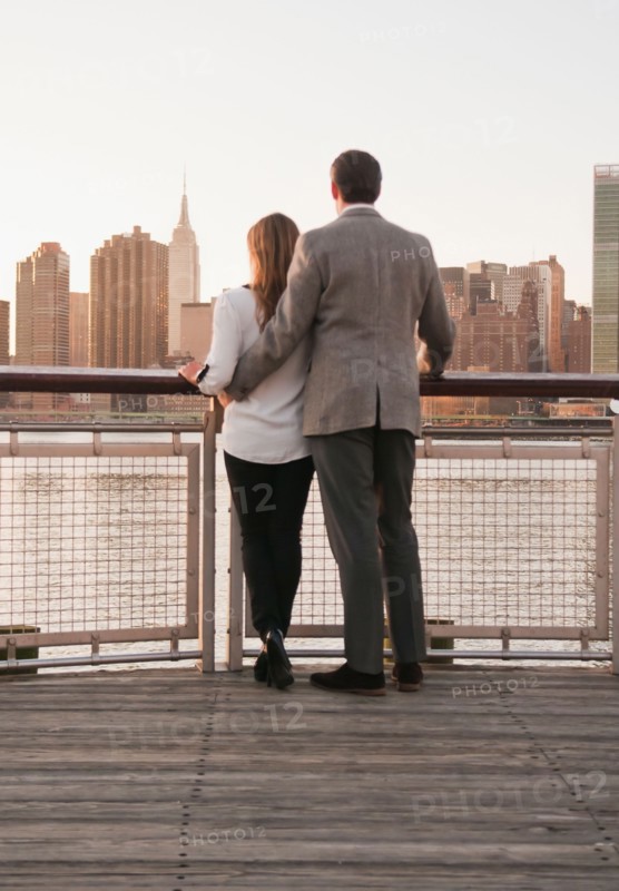 USA, New York, Long Island City, Rear view of young couple standing on boardwalk, Manhattan skyline in background. Photo : Daniel Grill