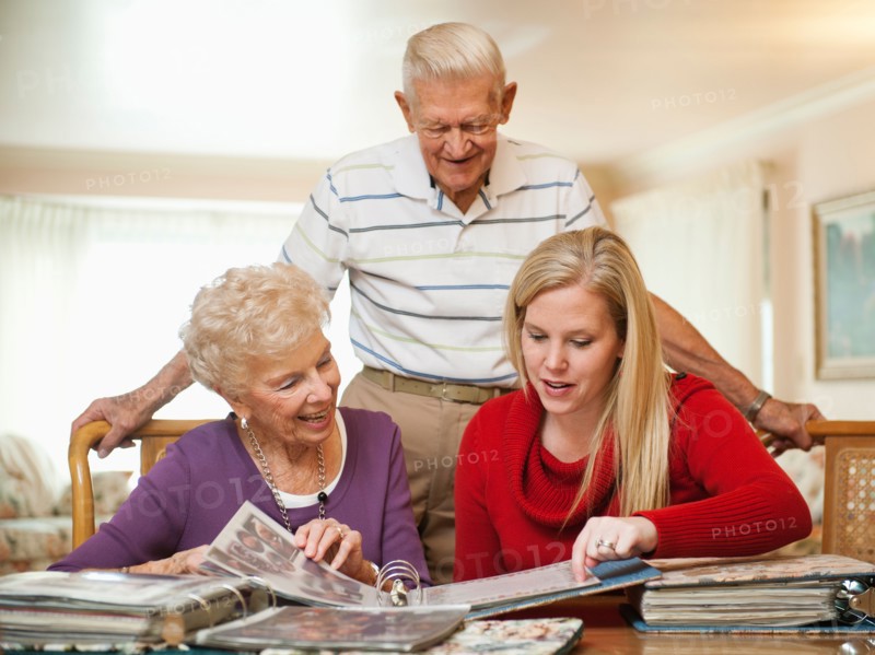 Senior couple and mid adult woman watching family scrapbooks.