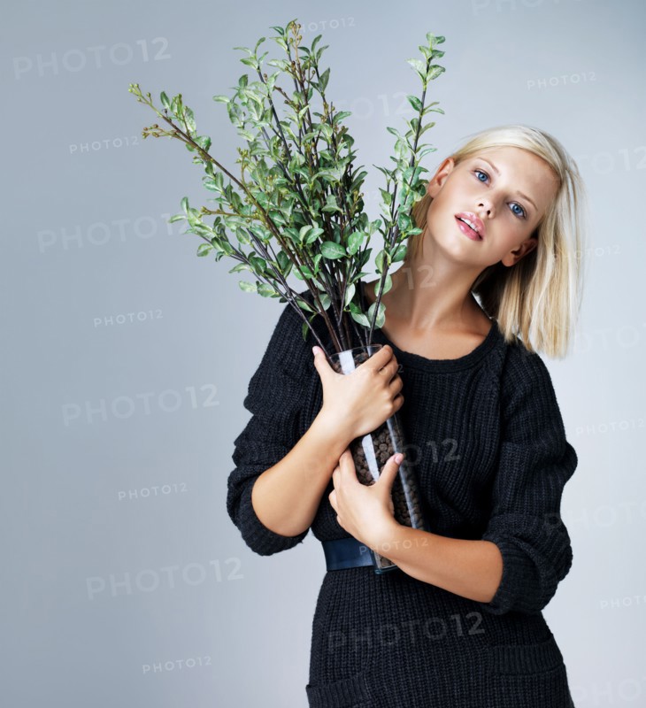 Young woman holding vase with green twigs, studio shot. Photo : Yuri Arcurs