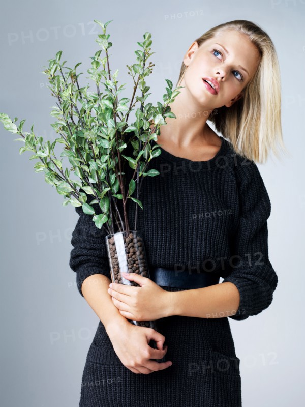 Young woman holding vase with green twigs, studio shot. Photo : Yuri Arcurs