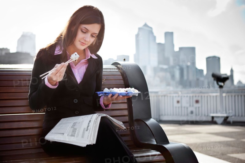 USA, Seattle, Young businesswoman eating sushi and reading newspaper. Photo : Take A Pix Media