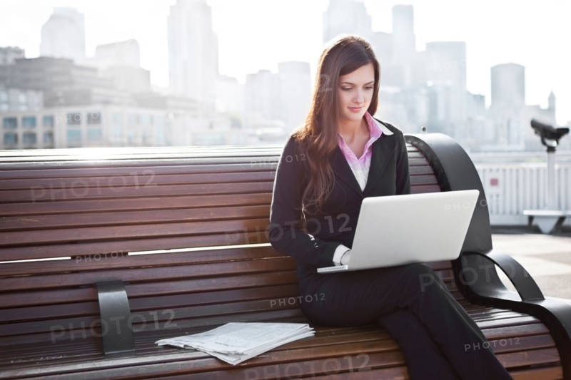 USA, Seattle, Young businesswoman working on laptop on bench. Photo : Take A Pix Media