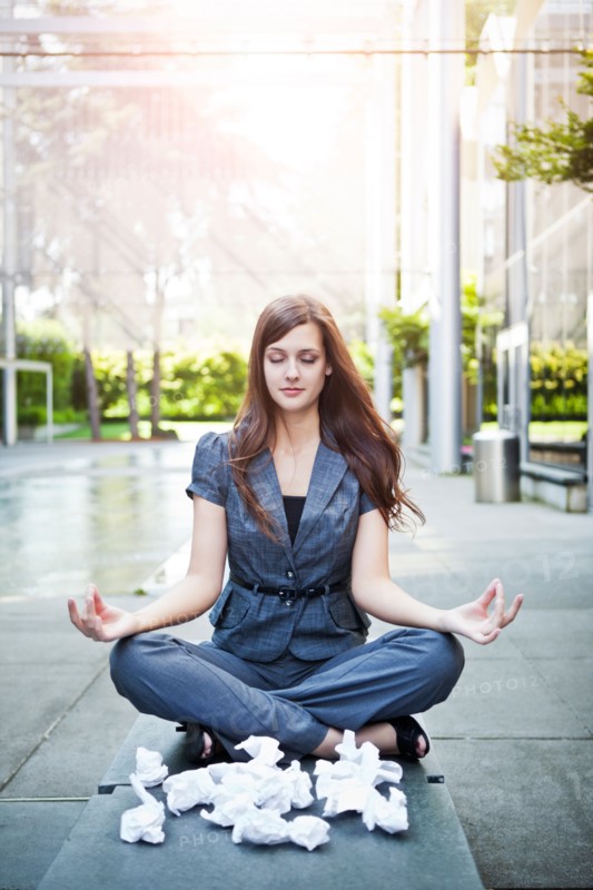 USA, Seattle, Young businesswoman meditating in front of crumbled paper balls. Photo : Take A Pix Media
