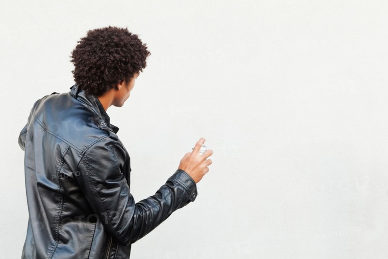 Man holding spray paint against white wall, studio shot. Photo : Sarah M. Golonka