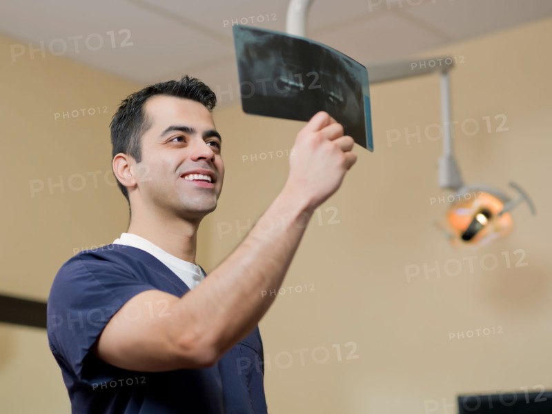 Smiling dentist in surgery checking x-ray . Photo : Dan Bannister