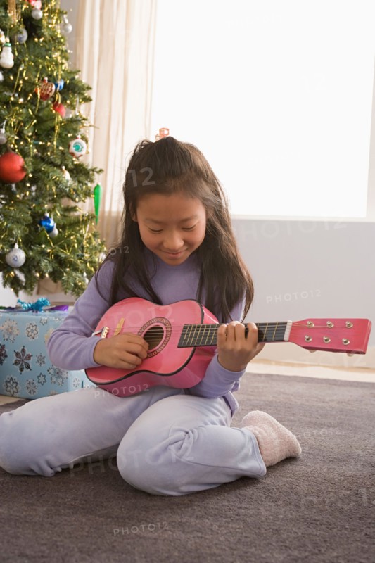Girl (10-11) playing guitar, Christmas tree in background. Photo : Rob Lewine