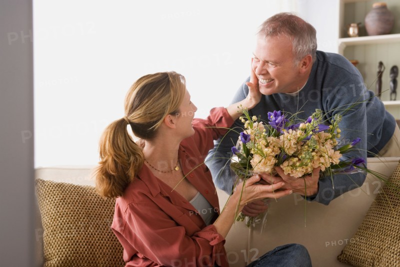 Senior man giving flowers to woman sitting on sofa. Photo : Rob Lewine