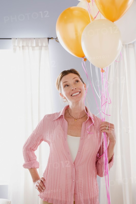 Smiling mature woman holding balloons. Photo : Rob Lewine