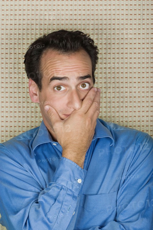Studio portrait of mid adult man covering mouth with hand. Photo : Rob Lewine