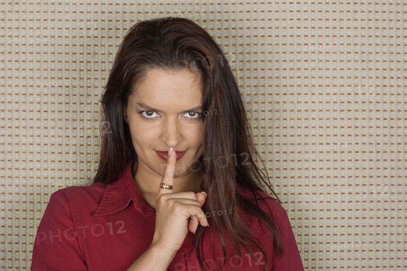 Studio portrait of mid adult woman with finger on lips. Photo : Rob Lewine