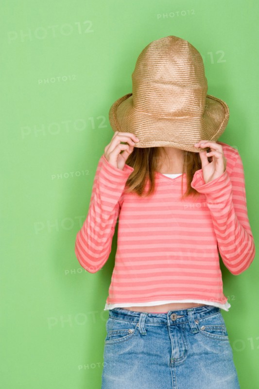 Studio portrait of teenage (16-17) girl covering face with hat. Photo : Rob Lewine
