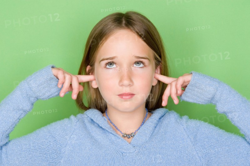 Studio shot portrait of teenage girl with fingers in ears, head and shoulders. Photo : Rob Lewine