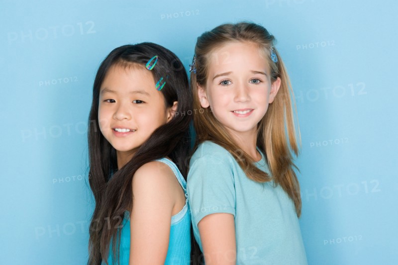 Studio shot portrait of two teenage girls standing back to back, head and shoulders. Photo : Rob Lewine