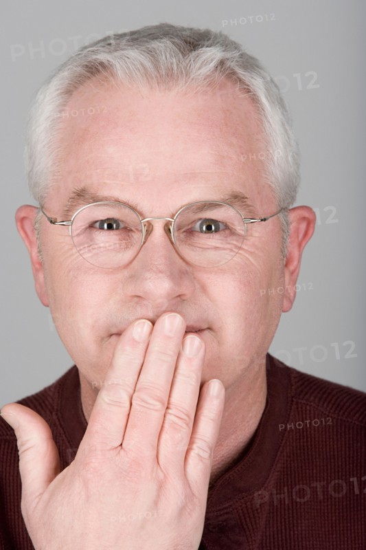 Studio shot portrait of senior man with hand covering mouth, close-up. Photo : Rob Lewine
