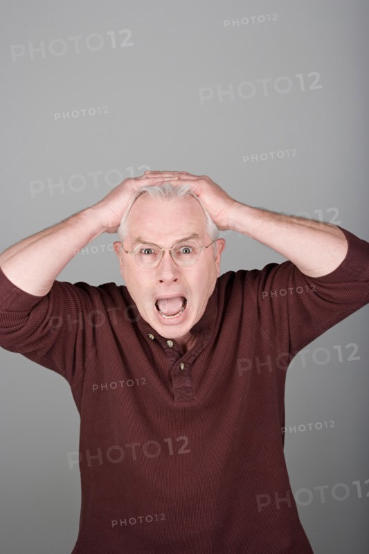 Studio shot portrait of senior man with head in hands and open mouth, waist up. Photo : Rob Lewine