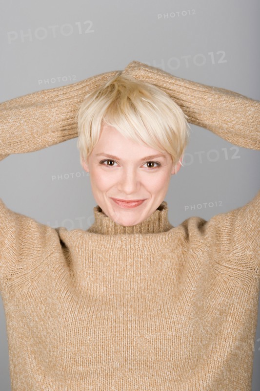 Studio shot portrait of mid adult woman with hands behind head, head and shoulders. Photo : Rob Lewine