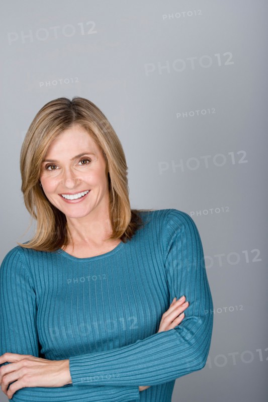 Studio shot portrait of mature woman with arms crossed, head and shoulders. Photo : Rob Lewine